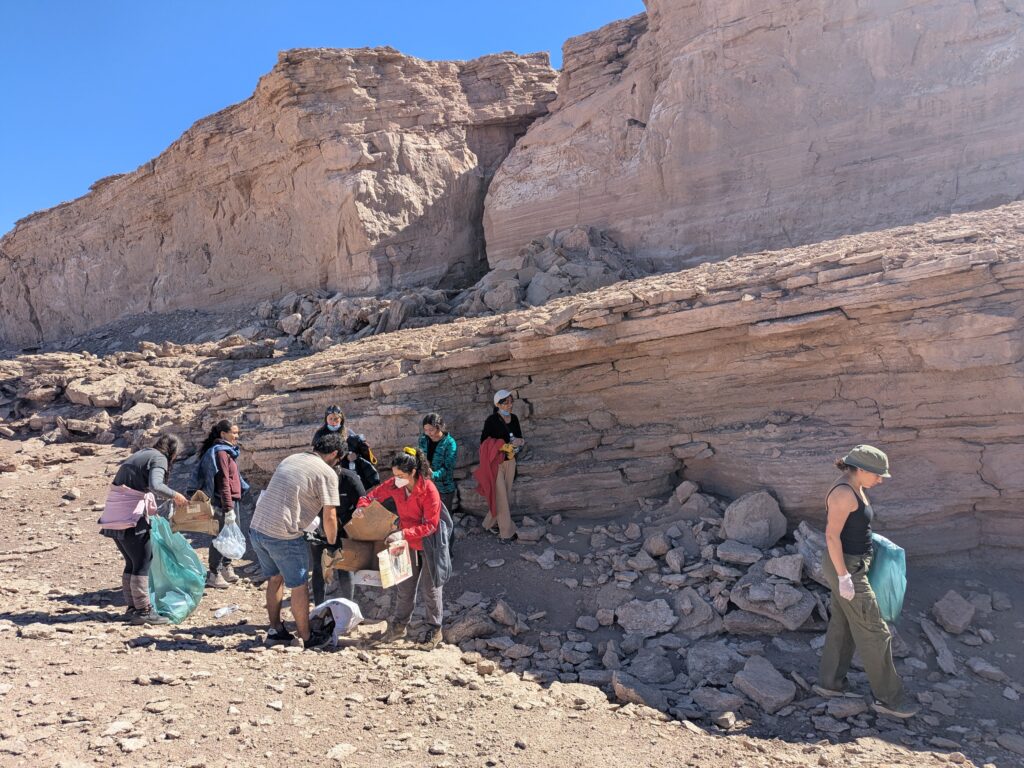 Limpieza Ambiental Grupo de voluntarios realizando limpieza ambiental en formación rocosa del desierto, recogiendo basura con bolsas verdes.